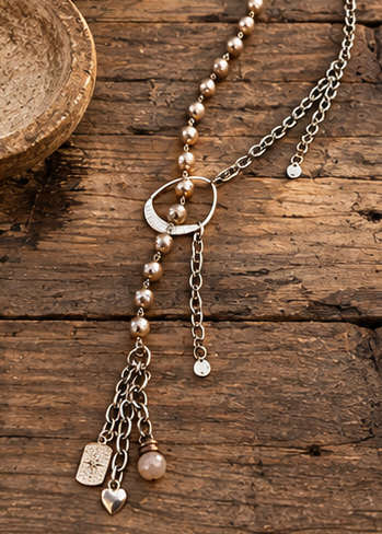 A bohemian-style lariat necklace with silver-tone chains, faux pearls, and charms, shown on a mannequin torso and in close-up detail shots against rustic wood and stone backgrounds.