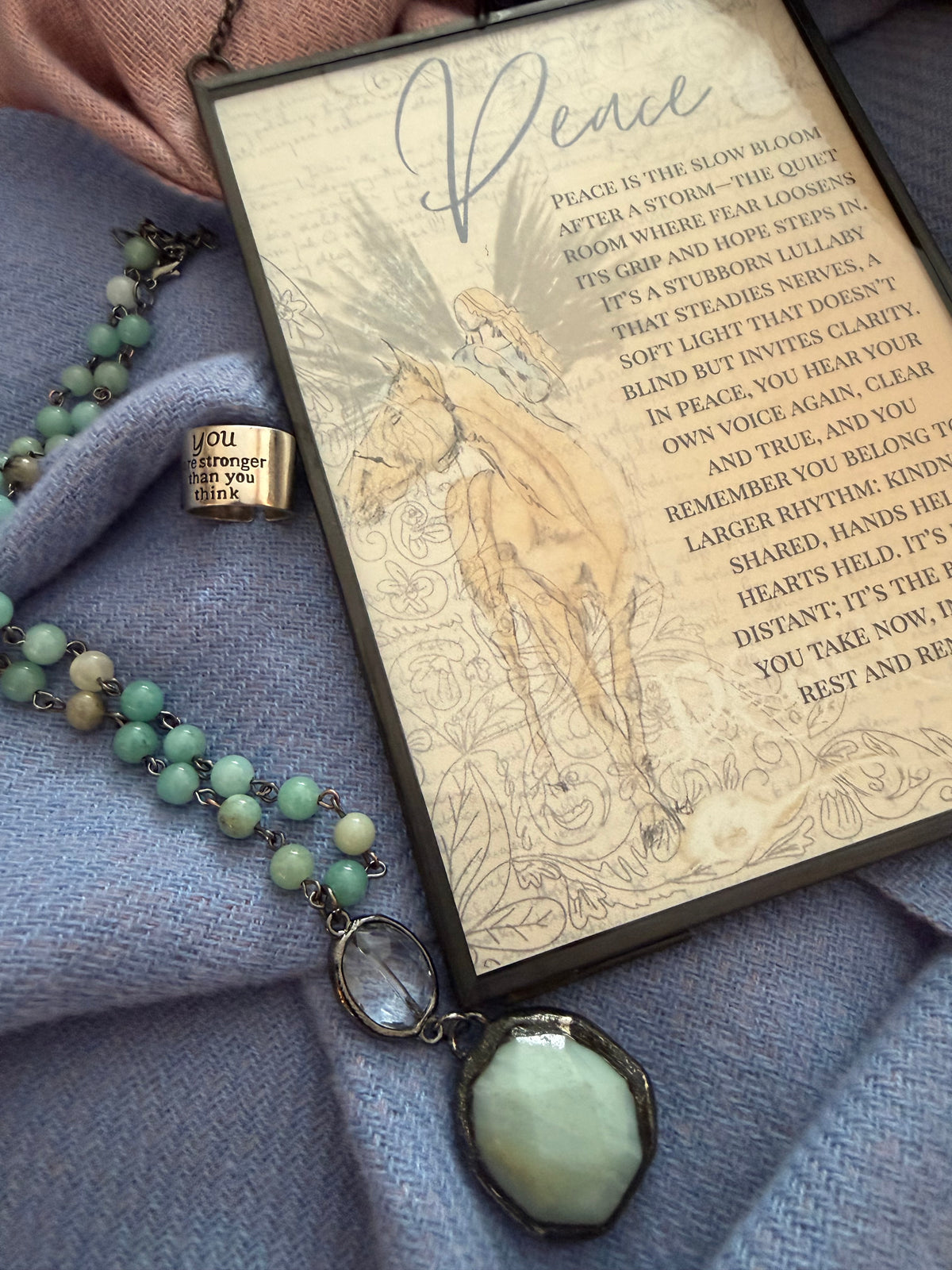 Vintage book with engraved text and illustration, green beaded necklace, and locket on a textured surface.