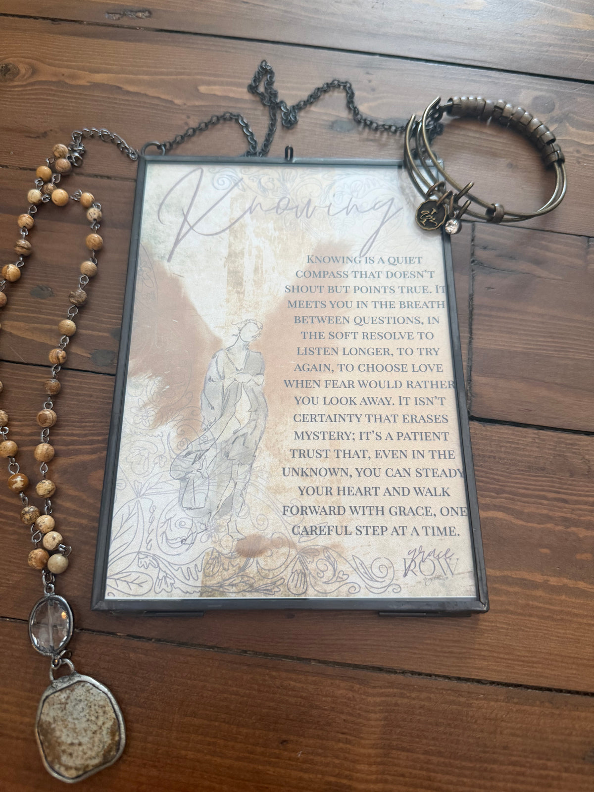 Decorative plaque with text and a rosary on a wooden surface