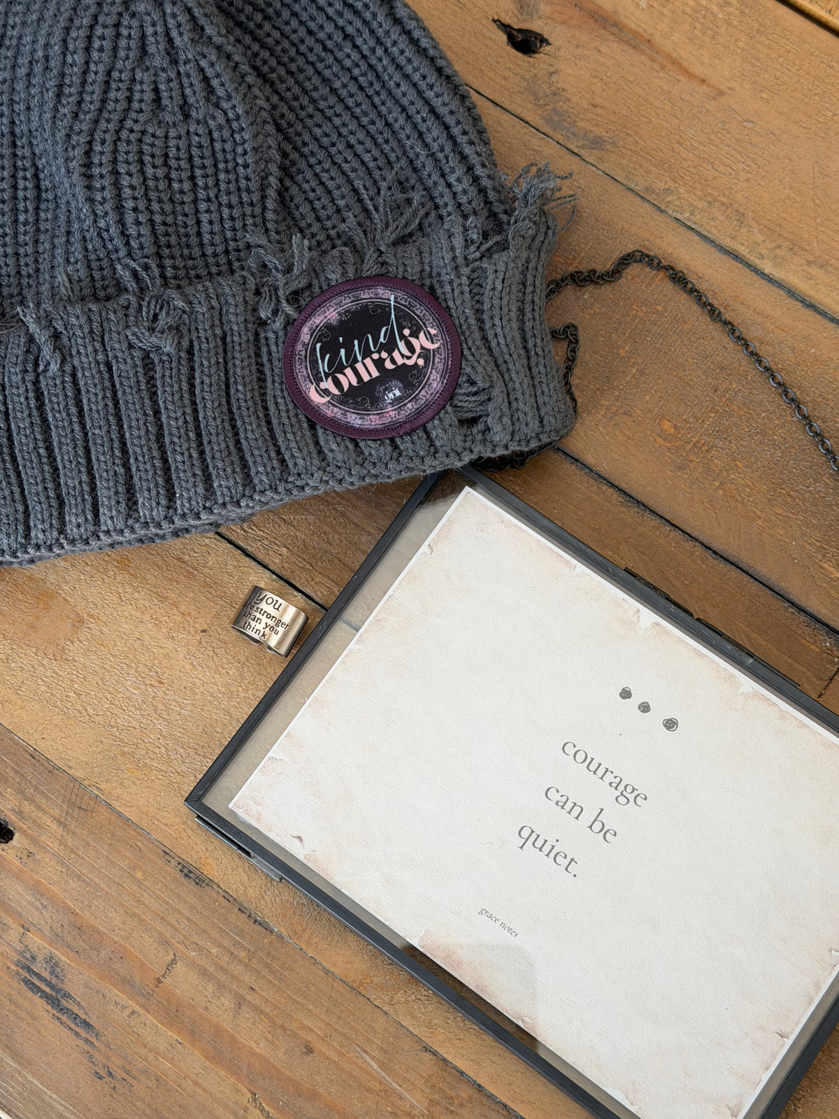 Gray knitted scarf with a purple button on a wooden surface next to an open book.