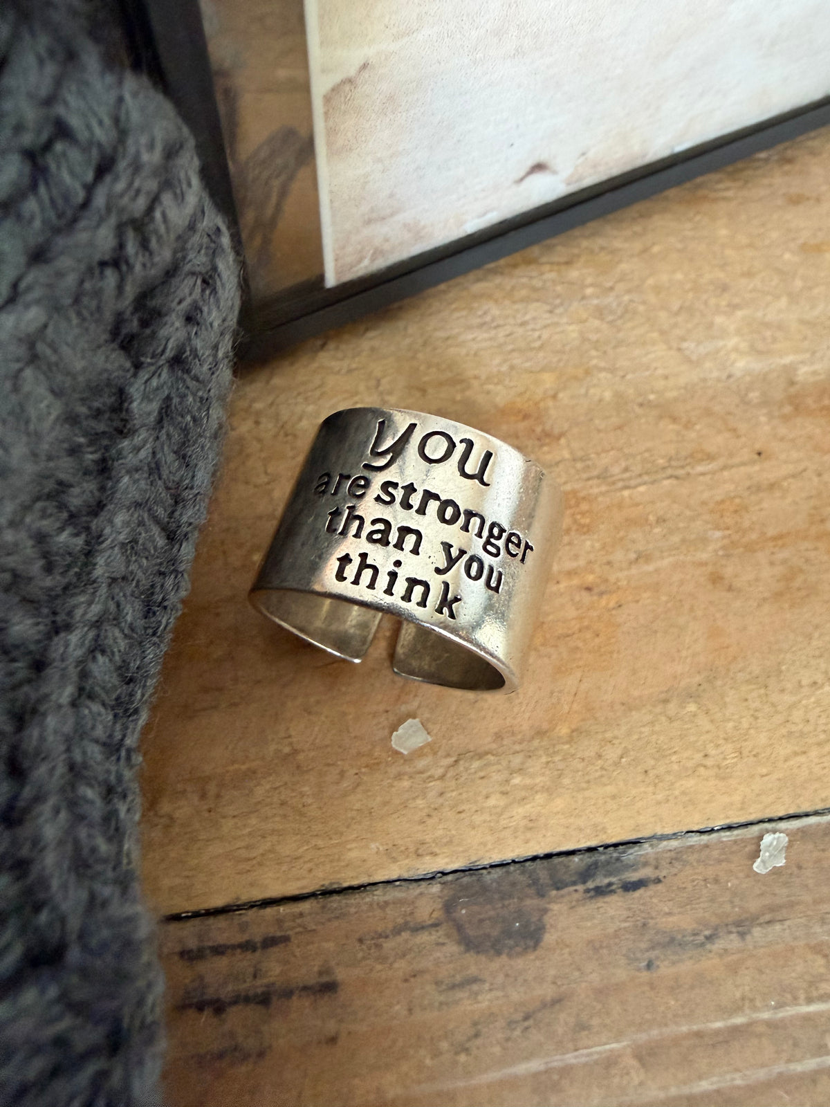Silver cuff bracelet with motivational quote on a wooden surface