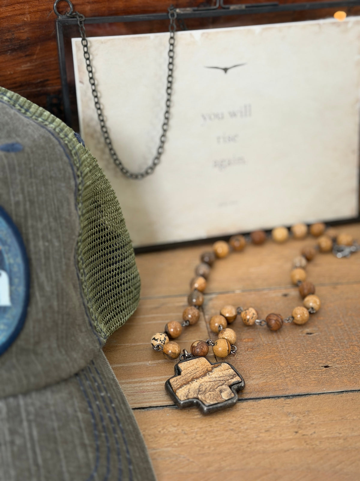 Wooden beaded necklace with a metal clasp on a wooden surface next to a cap and paper.